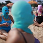 Women, wearing nylon masks, rest on the shore during their visit to a beach in Qingdao