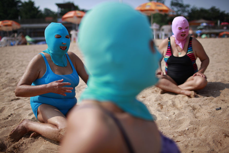 Women, wearing nylon masks, rest on the shore during their visit to a beach in Qingdao