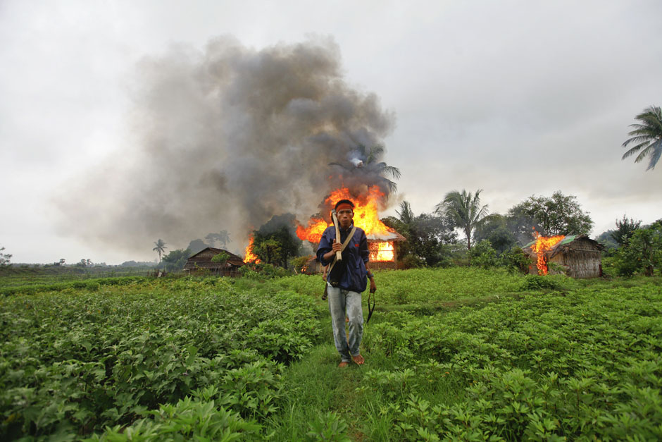 An ethnic Rakhine man holds homemade weapons as he walks in front of houses that were burnt during fighting between Buddhist Rakhine and Muslim Rohingya communities in Sittwe