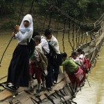 Students hold on to side steel bars of a collapsed bridge as they cross a river to get to school at Sanghiang Tanjung village in Lebak regency