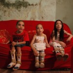 The children of the Amor Divino family, Dhones, Izabely and Samille, sit on their couch in Sao Paulo