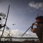 Indigenous people point their bows and arrows at a police helicopter flying over the occupied barrier of the Belo Monte Dam's construction site in Vitoria do Xingu, near Altamira