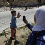 A Jewish boy lifts his hand to prevent a Palestinian from taking his picture near a police barrier cordoning off a building in Hebron