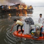 Residents paddle their makeshift boat to safety as fire engulfs houses at a slum community in Manila