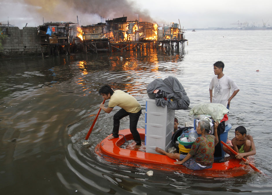 Residents paddle their makeshift boat to safety as fire engulfs houses at a slum community in Manila