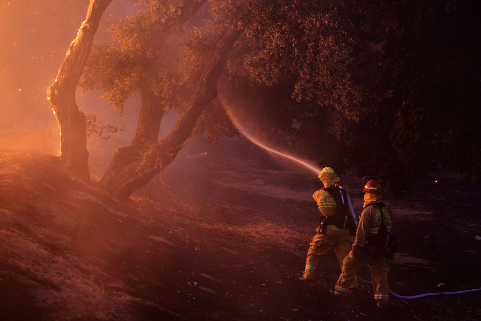 Firefighters spray water near a burning house in the Twin Pines Road area at the Silver Fire near Banning, California.