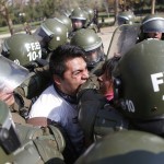 A student protester bites a riot policeman while being detained during a riot at a rally demanding Chile's government reform the education system in Santiago