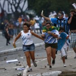 A family with soccer match tickets runs for cover as they come between law enforcement troops and protesters during a demonstration outside the stadium in Salvador