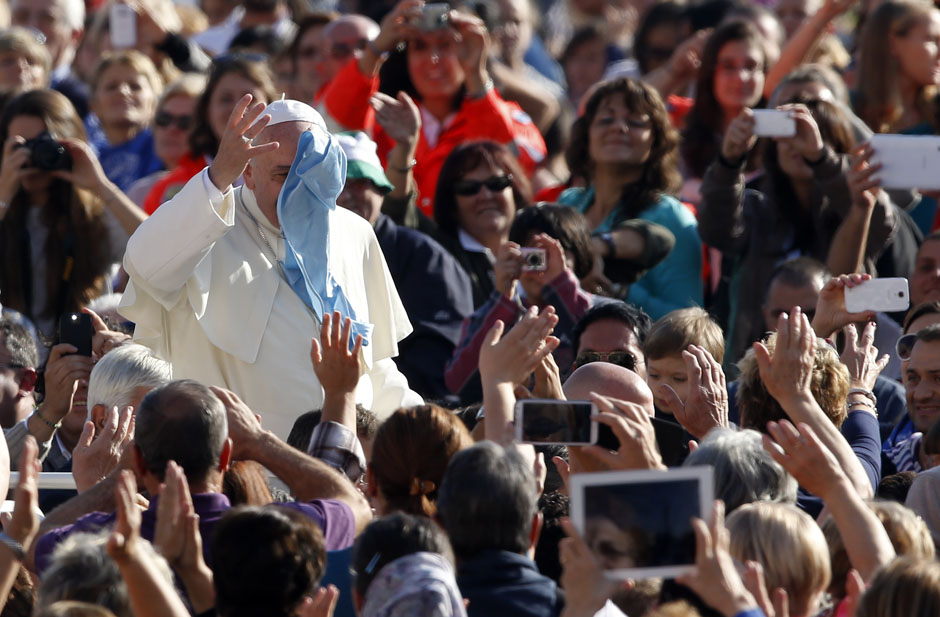 Pope Francis waves as he tries to grab handkerchief thrown by faithful as he arrives to lead his Wednesday general audience in Saint Peter's square at the Vatican