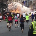 Runners continue to run towards the finish line as an explosion erupts at the finish line of the Boston Marathon