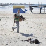 A man carries a child as another lies dead after two explosions on a beach in Gaza.