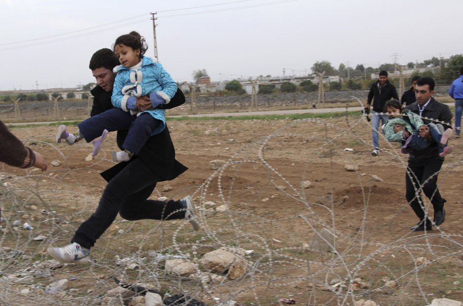 Syrians jump over barbed wire as they flee from the Syrian town of Ras al-Ain to the Turkish border town of Ceylanpinar