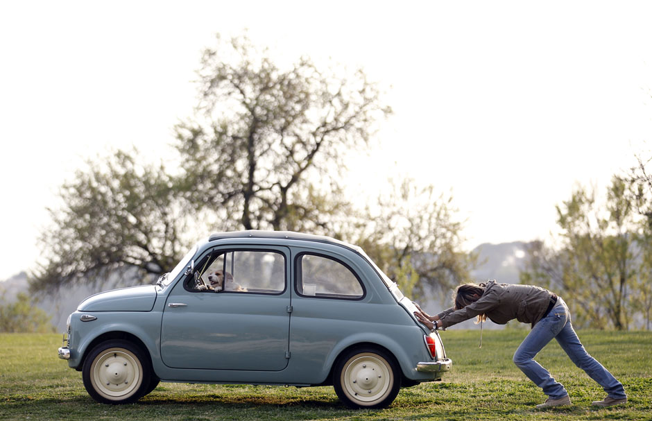 Woman pushes her Fiat 500 car as her dog sits inside, in neighbourhood of Rome