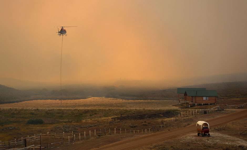 A firefighting helicopter fills a bucket of water in heavy smoke as the North Merna wildfire burns in the Bridger National Forest west of the town of Pinedale in Sublette County, Wyoming