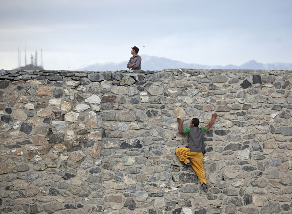 An Afghan man takes a shortcut by climbing a wall, at a hilltop in Kabul