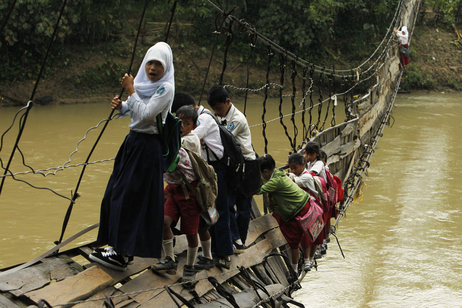 Students hold on to side steel bars of a collapsed bridge as they cross a river to get to school at Sanghiang Tanjung village in Lebak regency