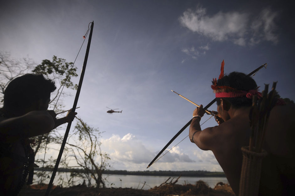 Indigenous people point their bows and arrows at a police helicopter flying over the occupied barrier of the Belo Monte Dam's construction site in Vitoria do Xingu, near Altamira