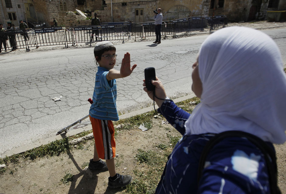 A Jewish boy lifts his hand to prevent a Palestinian from taking his picture near a police barrier cordoning off a building in Hebron