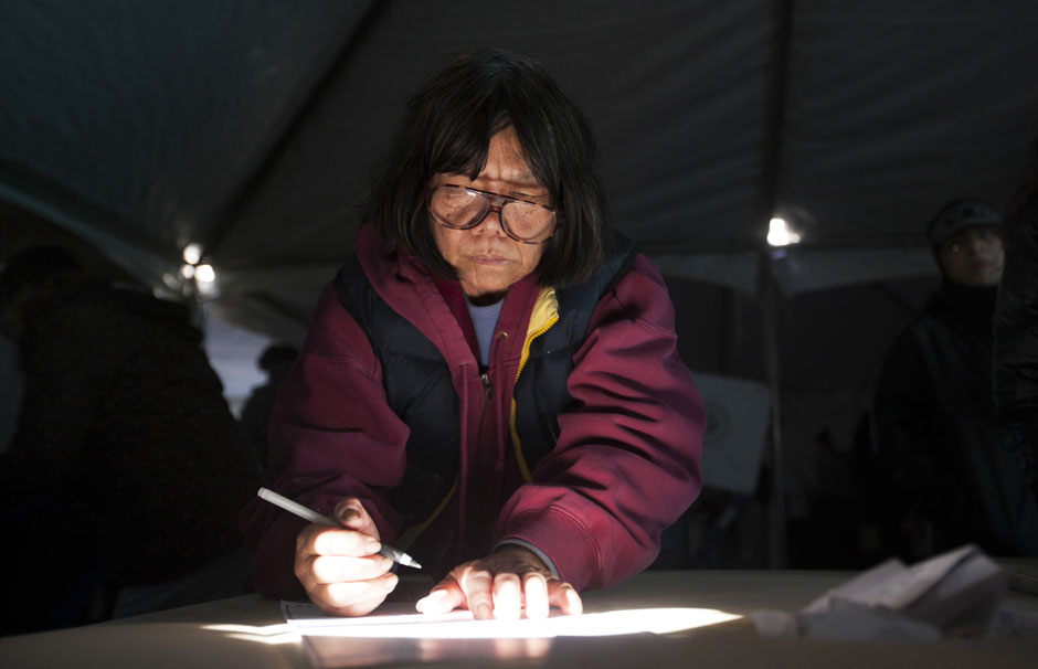 Woman uses shaft of sunlight to see her ballot as she votes in polling site during U.S. presidential election in New York