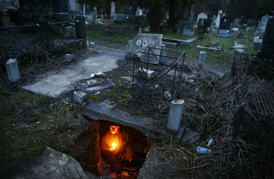 Bratislav Stojanovic, a homeless man, hold candles as he sits in a tomb where he lives in southern Serbian town of Nis