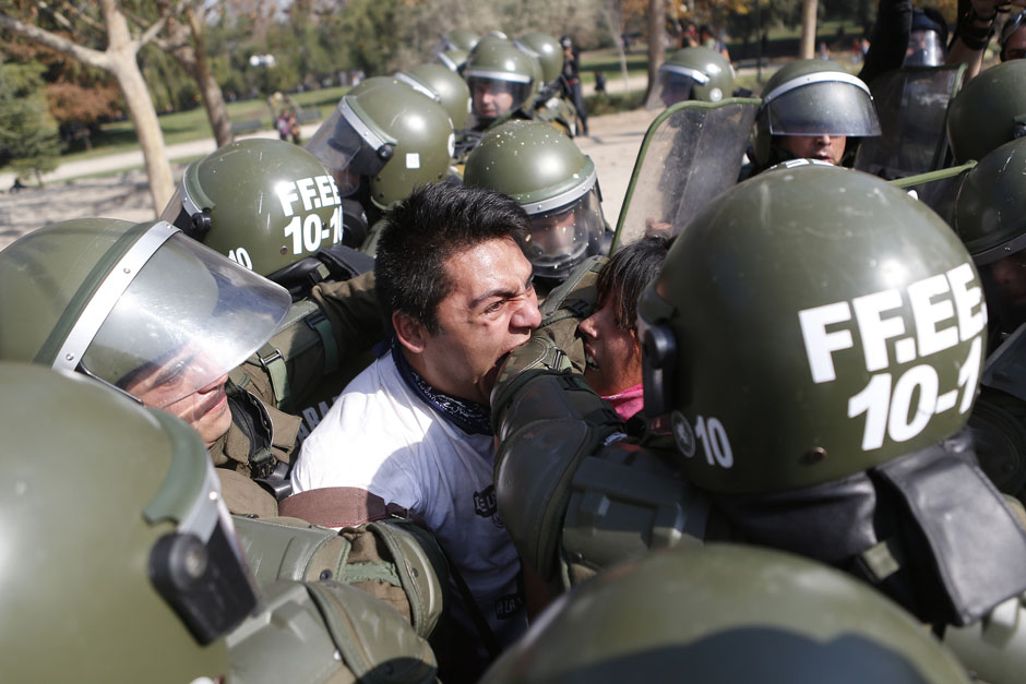 A student protester bites a riot policeman while being detained during a riot at a rally demanding Chile's government reform the education system in Santiago