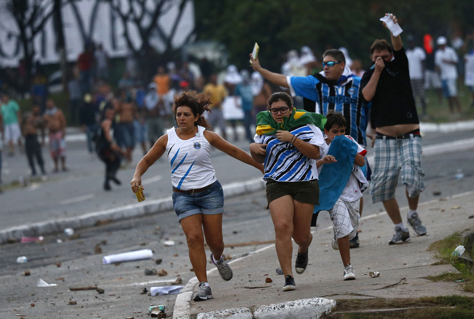 A family with soccer match tickets runs for cover as they come between law enforcement troops and protesters during a demonstration outside the stadium in Salvador