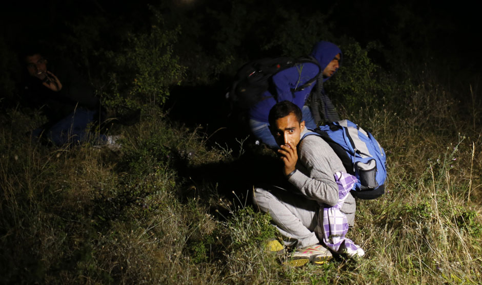 Migrants sit on the ground after being apprehended by the Serbian border police, having illegally entered the country from Macedonia, near Presevo