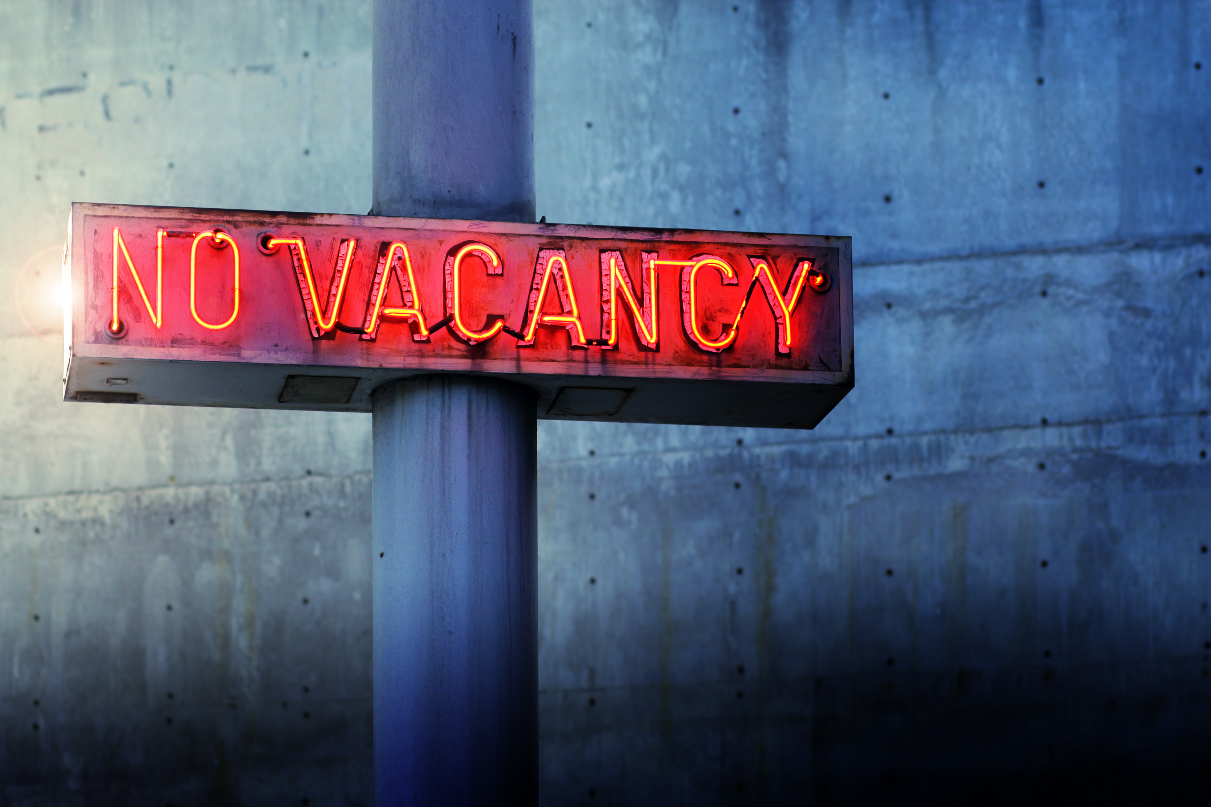 Glowing retro neon 'no vacancy' sign against blue wall