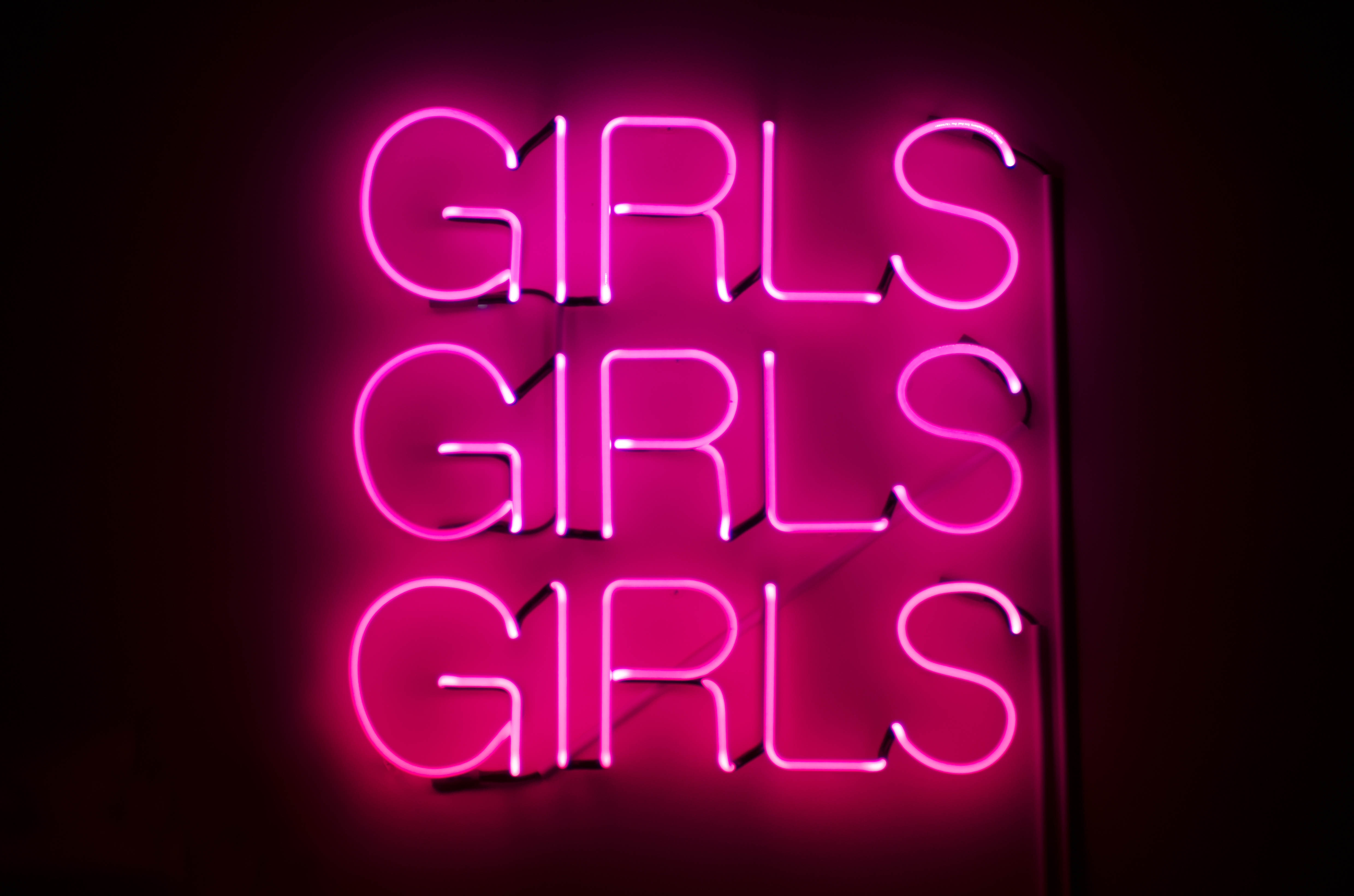 Girls Girls Girls sign glows in racy pink neon against dark night background