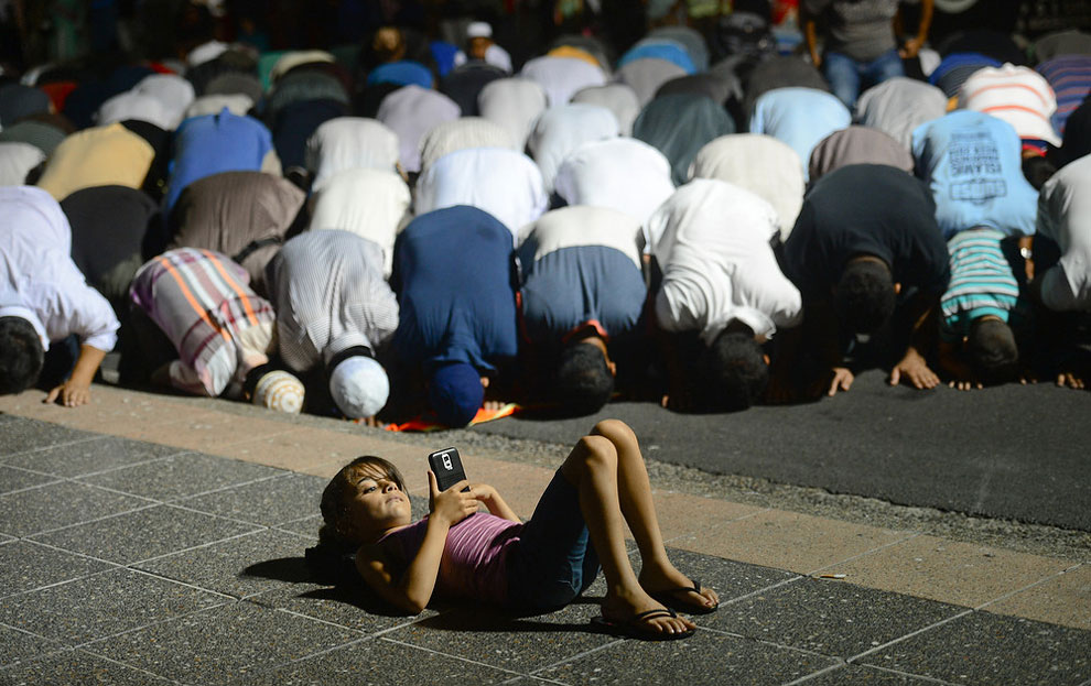 Call to Prayer. A young girl plays on her phone in front of Muslim men as they take evening prayer in Lakemba. (Photo by Jeremy Piper:Australian Life Prize 2015)