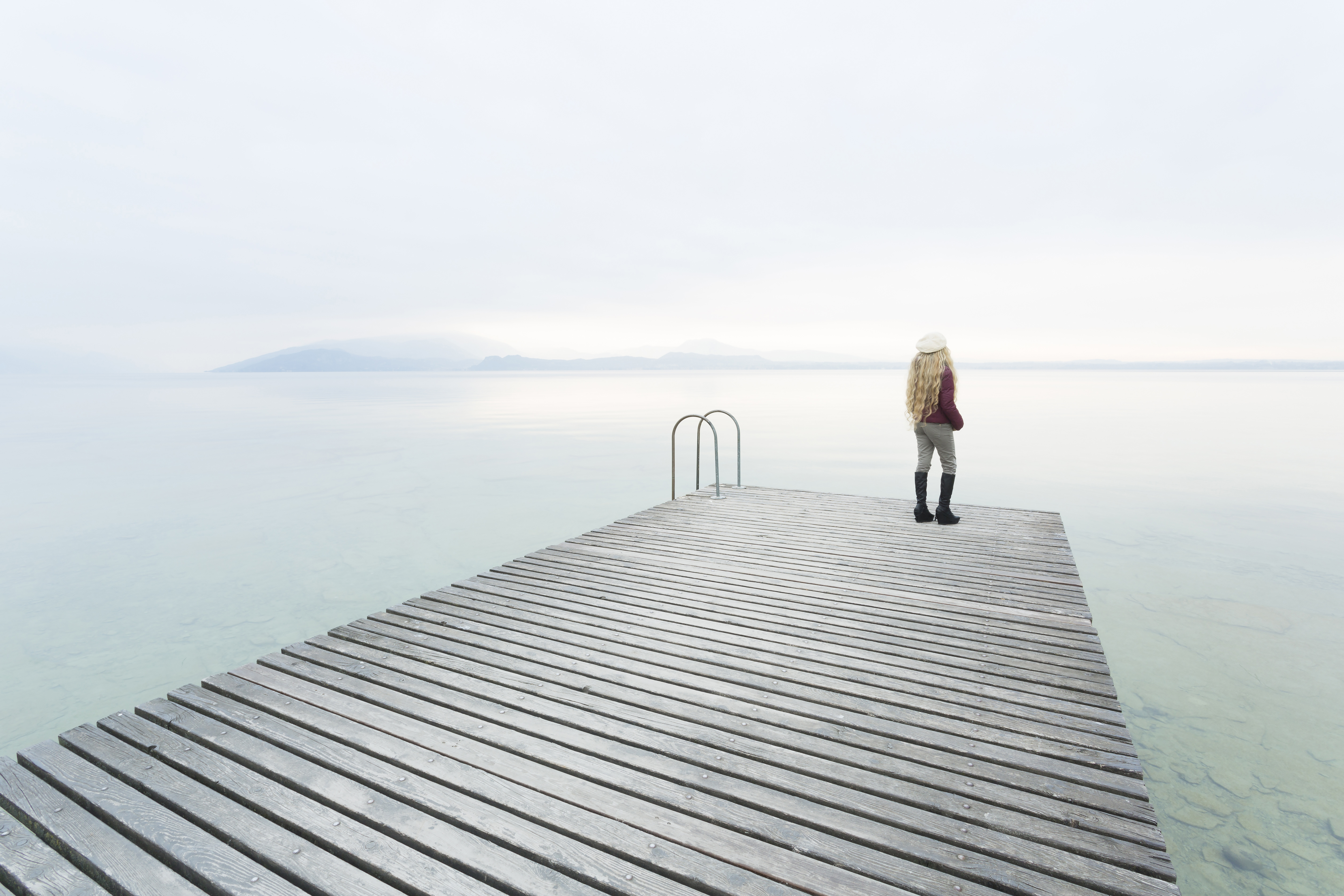 Young woman with long blond hair with hat on the dock of a lake