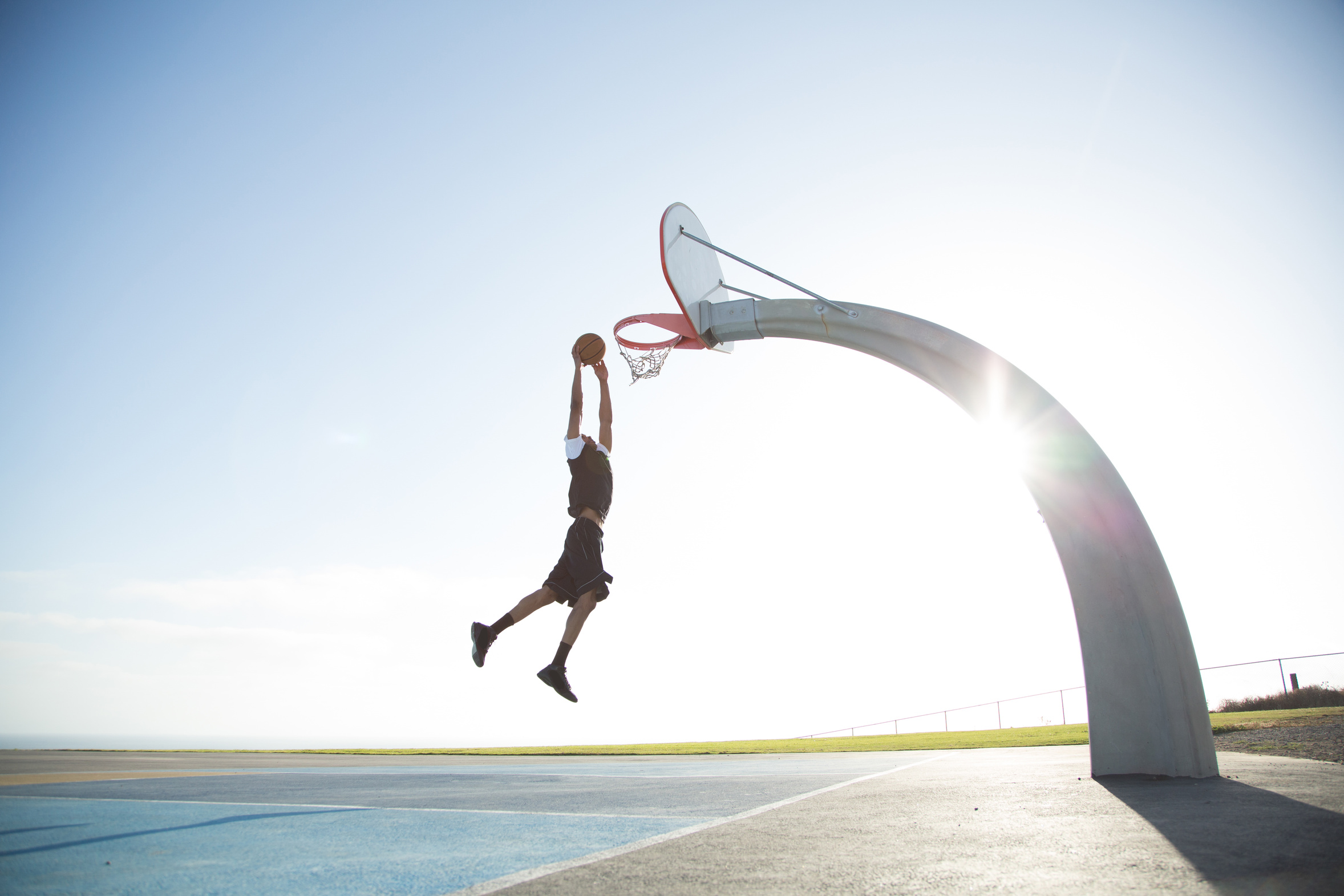 A mid 20's black male plays basketball in a beautiful location in southern california that overlooks the ocean.  A fitness athlete excercises by shooting hoops in a park that overlooks the pacific ocean in Los Angeles. Shots, hoops, dunks, slamdunk