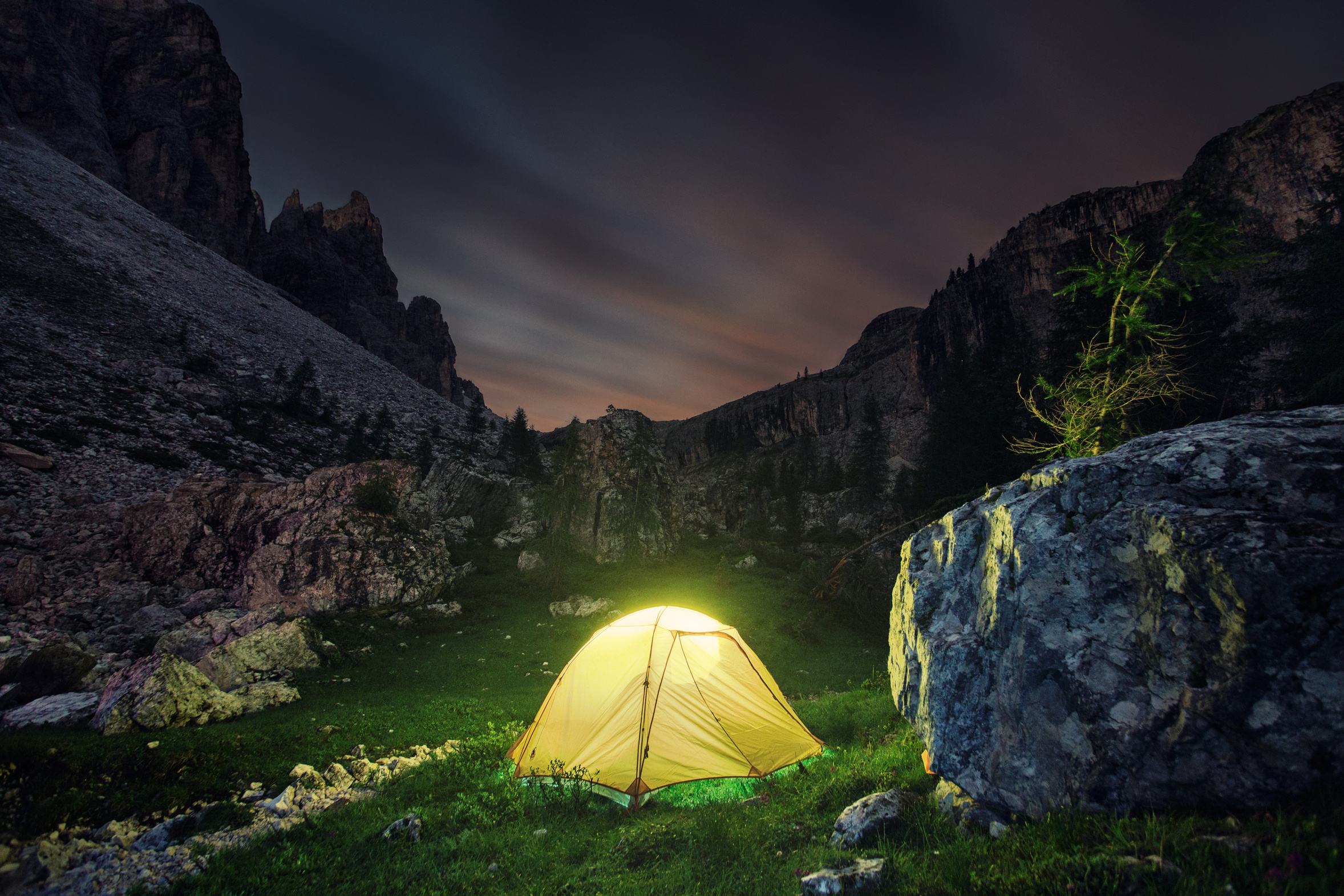 Tent illuminated at night pitched by rocky mountains
