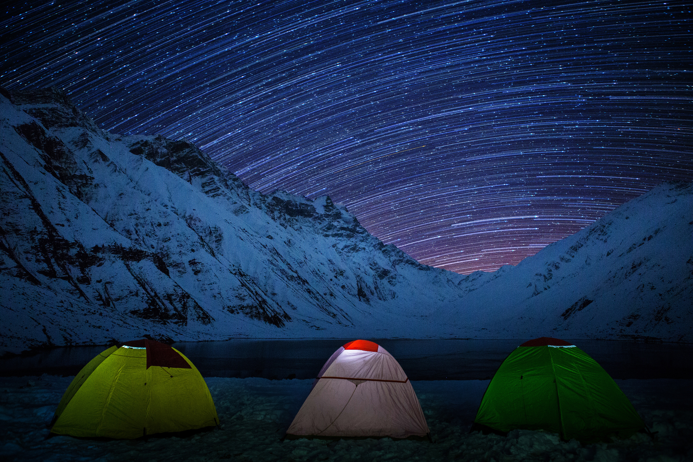 Tents at the shore of Lake Saiful Muluk and star trails in the sky in Pakistan.