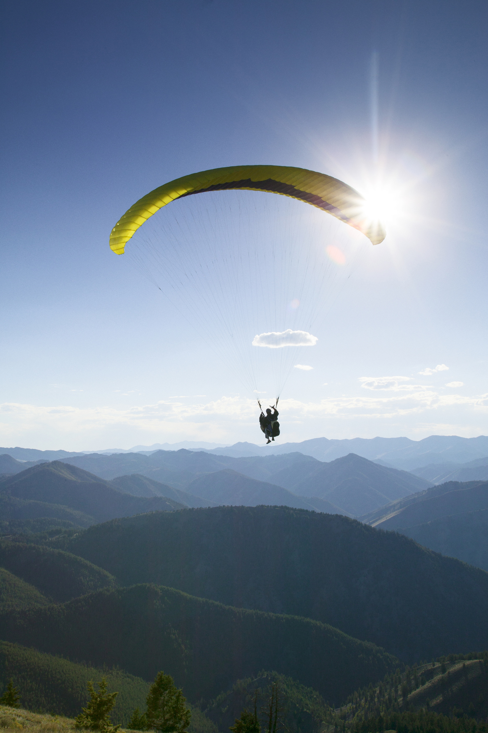 Silhouette person paragliding over mountains against bright sky