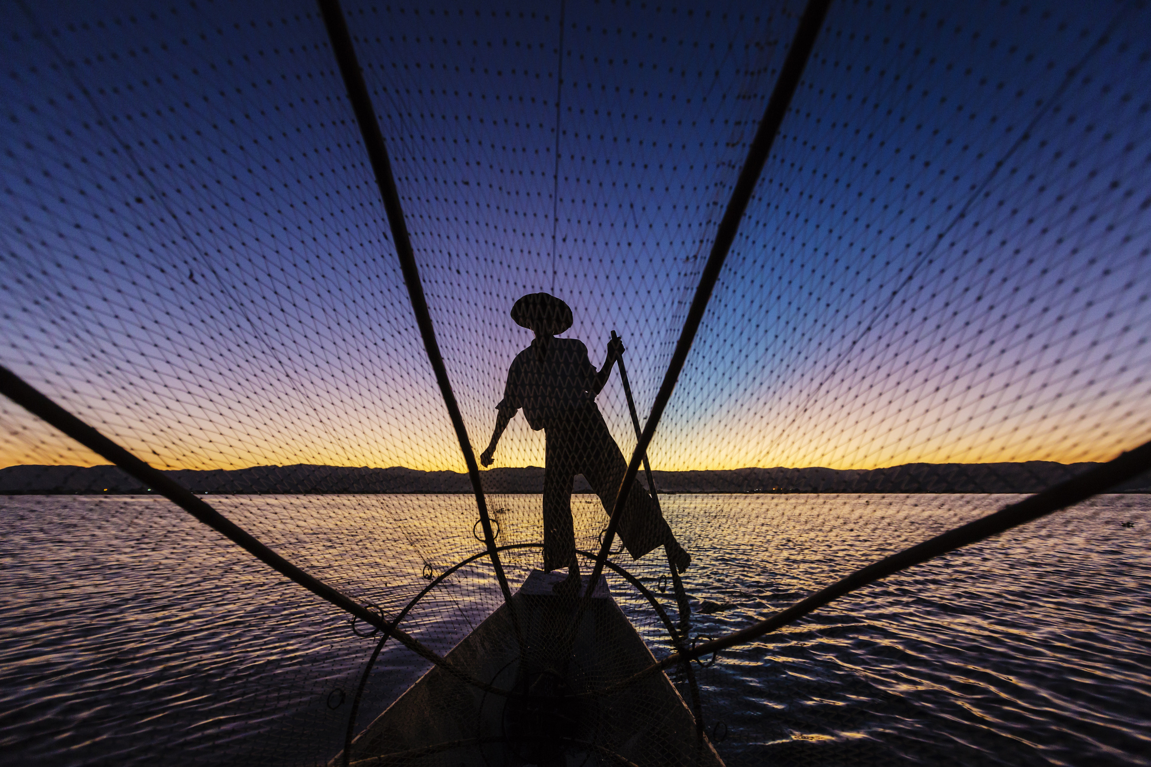 Silhouette of fisherman rowing canoe on water