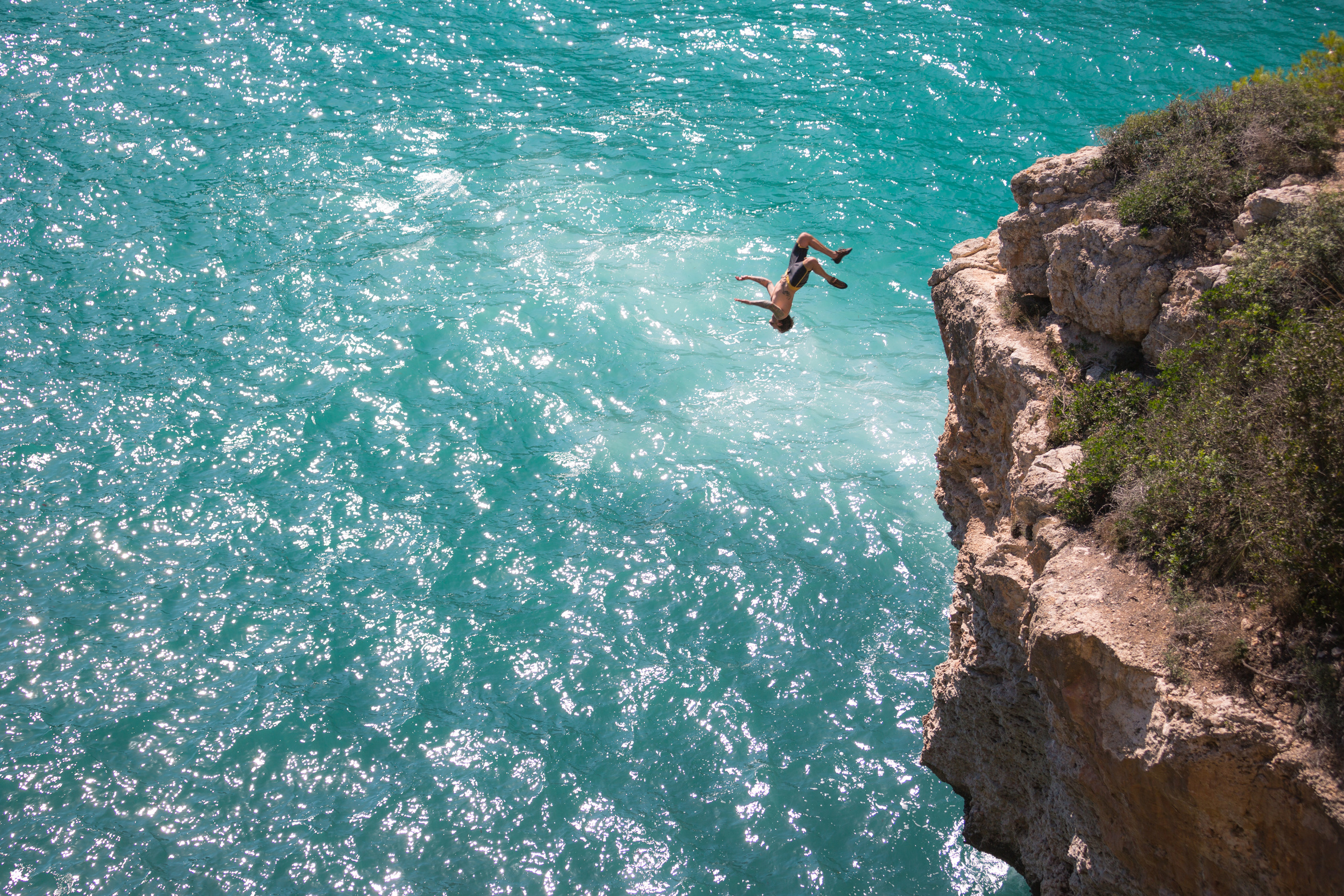 Man jumping upside down from cliff to sea, full frame