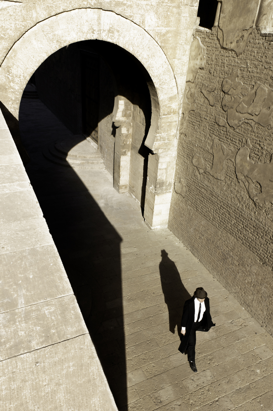 Man in suit with fedora walking through ancient ruins