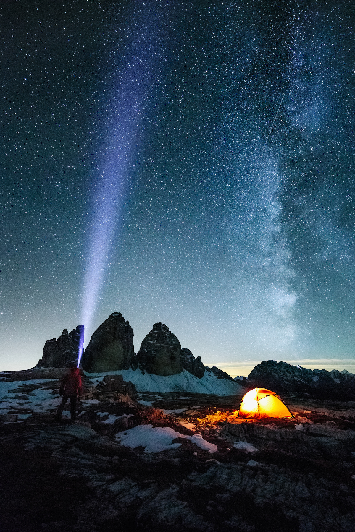 male adventurer with strong headlamp beside illuminated red orange under the milky way