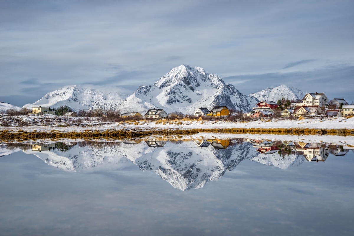reflection of snow capped mountains and buildings in lake, norway