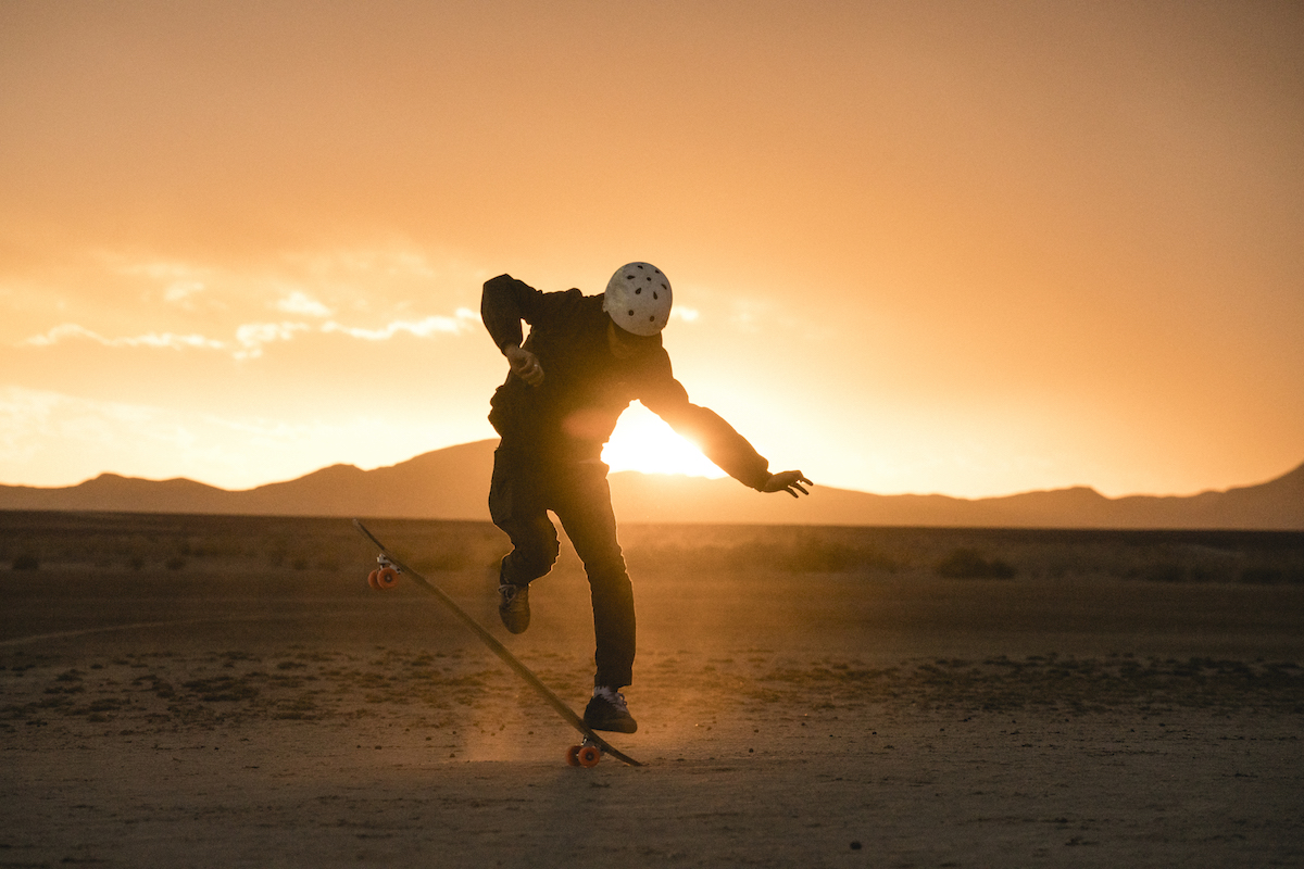 Full length of man performing stunt with skateboard on field against sky during sunset
