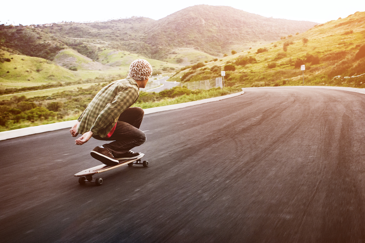 Young Man Long Boarding Down Road