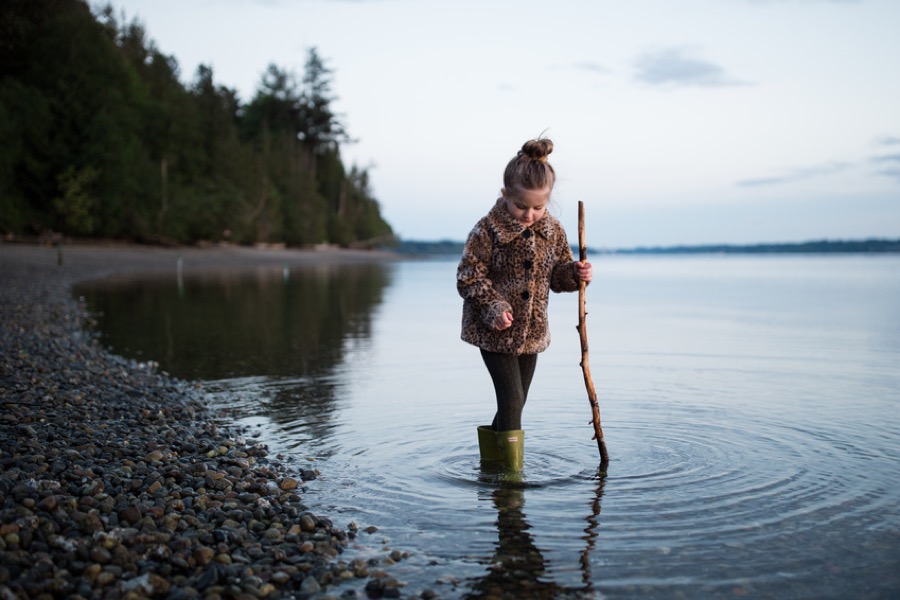 Young girl standing in water by lakeside holding stick